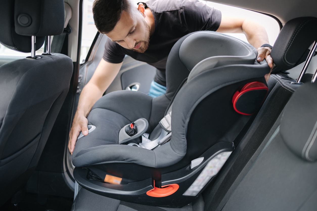 Man installing a child car seat in car at the back seat