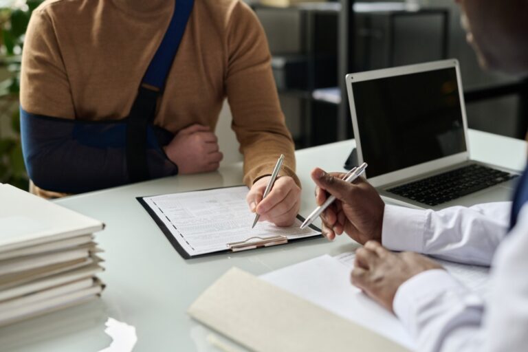 individual in a sling signing medical document alongside doctor