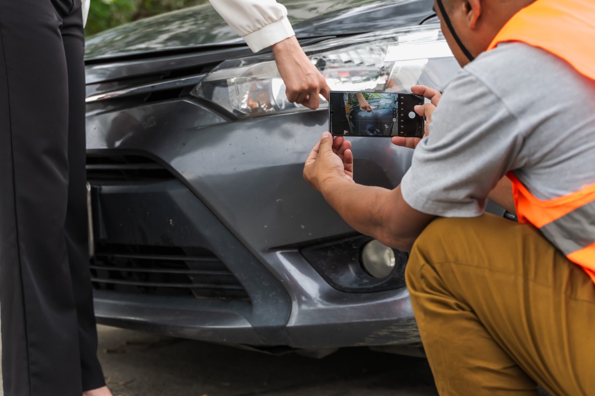 man taking image of vehicle damage after an accident